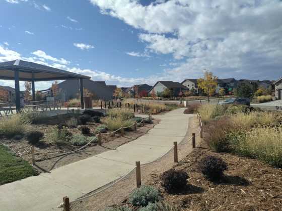 Native xeric planting at Explorer Park in Loveland, Colorado, bordered by rope fence along sidewalk with shade structure in background